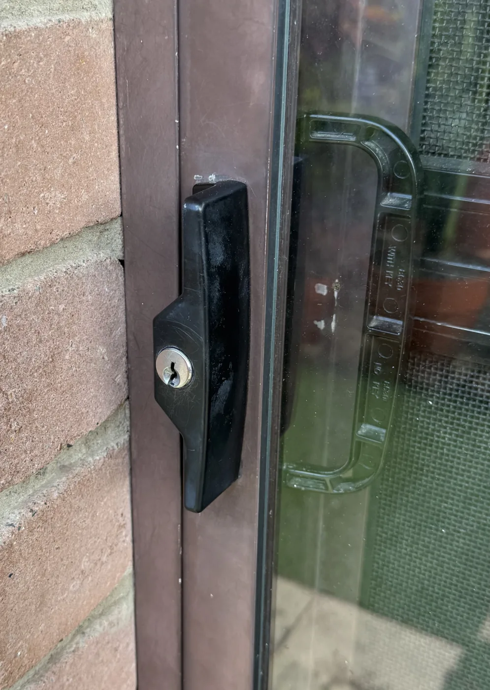 Black Whitco low-profile sliding door lock on a brown aluminium G. James glass door, with the screen door handle visible behind it